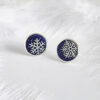 These frosted enamel snowflake earrings are made of 925 sterling silver and are displayed against a feather background.