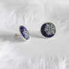 These frosted enamel snowflake earrings are made of 925 sterling silver and are displayed against a feather background.