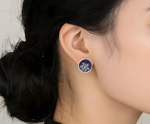 Winter Spritel Close-up of a model wearing the Winter Spirit snowflake earrings. The frosted enamel design complements a cozy winter look, showing the elegant scale and artistic detail of the jewelry.