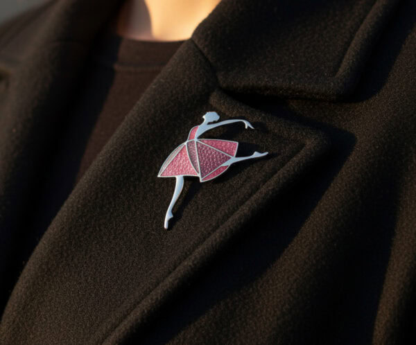 The "Dancing Moments" Champlevé enamel ballerina brooch pinned to the lapel of a black wool coat, showing the styling and scale of the piece worn in natural sunlight.