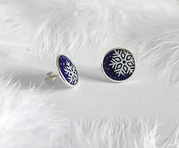Winter Sprite1 These frosted enamel snowflake earrings are made of 925 sterling silver and are displayed against a feather background.