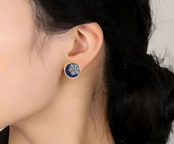 Winter Spriter Close-up of a model wearing the Winter Spirit snowflake earrings. The frosted enamel design complements a cozy winter look, showing the elegant scale and artistic detail of the jewelry.