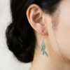 A natural light portrait of a woman adorned with the leaf-shaped Willow Green Plique-à-jour earring. The translucent green enamel mimics sunlit spring foliage, adding a subtle touch of nature’s radiance to her elegant profile.