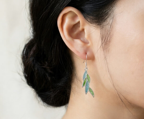 A natural light portrait of a woman adorned with the leaf-shaped Willow Green Plique-à-jour earring. The translucent green enamel mimics sunlit spring foliage, adding a subtle touch of nature’s radiance to her elegant profile.