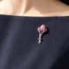Close-up of a 925 silver champleve enamel brooch in the shape of a pink and purple balloon cluster. The artisan jewelry piece is pinned to the lapel of a navy blue dress worn by a model.