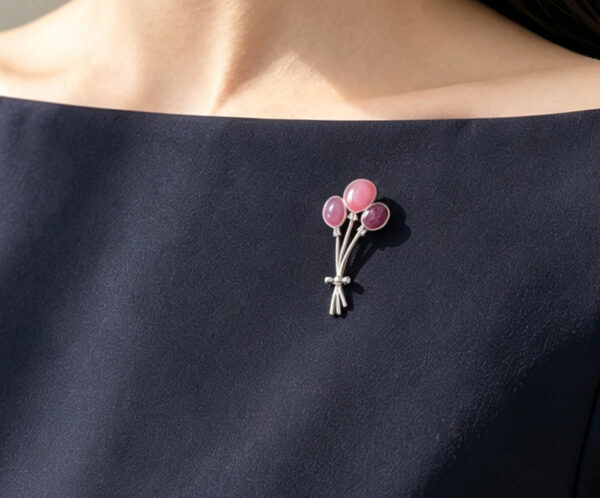 Close-up of a 925 silver champleve enamel brooch in the shape of a pink and purple balloon cluster. The artisan jewelry piece is pinned to the lapel of a navy blue dress worn by a model.