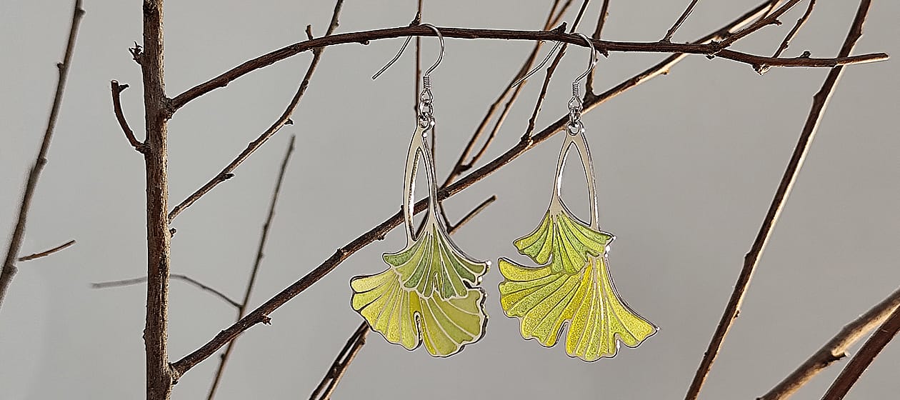 Delicate pair of earrings hanging gracefully on a branch, inspired by the shape of ginkgo leaves, showcasing intricate craftsmanship and vibrant colors.