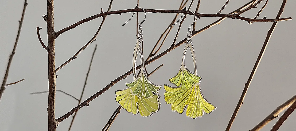Delicate pair of earrings hanging gracefully on a branch, inspired by the shape of ginkgo leaves, showcasing intricate craftsmanship and vibrant colors.
