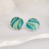 Handcrafted enamel stud earrings inspired by “Still waters run deep,” with blue-green tones and engraved silver. Elegant for daily wear or as a thoughtful gift.