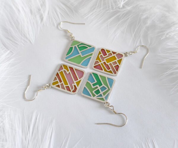 Two pairs of handcrafted plique-à-jour enamel earrings in square silver frames, featuring abstract line designs inspired by Chinese characters for “Peace” and “Joy,” with soft blue, pink, and golden hues glowing through openwork patterns, displayed on a white background with soft white feathers.