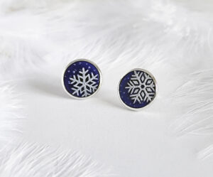 These frosted enamel snowflake earrings are made of 925 sterling silver and are displayed against a feather background.