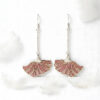 Poppy Grace Plique-à-jour enamel earrings in 925 sterling silver, featuring a delicate pink ginkgo-shaped fan design suspended on long silver chains, set against a blurry spring meadow background with soft sunlight.