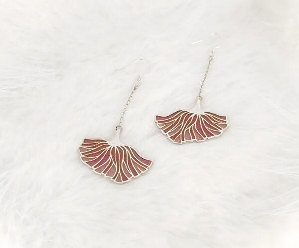 Poppy Grace Plique-à-jour enamel earrings in 925 sterling silver, featuring a delicate pink ginkgo-shaped fan design suspended on long silver chains, set against a blurry spring meadow background with soft sunlight.