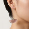 A close-up side profile of a model wearing the Poppy Grace Plique-à-jour enamel earrings. The light-as-wings pink enamel fans sway gracefully, catching the soft sunlight to reveal their semi-transparent texture against the model’s neck.